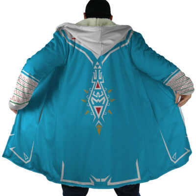 A person wears the Breath of Wild Zelda Dream Cloak Coat, a long blue hooded coat with intricate white and gold designs on the back and sleeves, inspired by fantasy video games. The coat is open to showcase its detailed patterns.