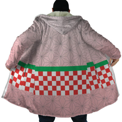 A person showcases the Nezuko Kamado Demon Slayer Dream Cloak Coat—a large, light pink coat with geometric patterns, a green stripe, and a red-and-white checkerboard design on the lower back—by holding it open.