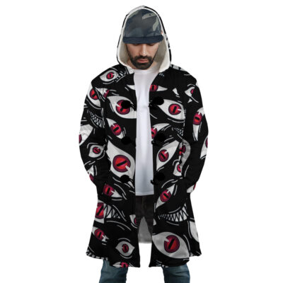 A man stands with hands in pockets, wearing the Pride Fullmetal Alchemist Dream Cloak Coat featuring a bold black, white, and red abstract eye and mouth design. He layers it over a hoodie and cap while looking down.