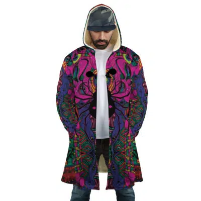 A man wearing the Trippy Mystic Faces Hisoka Hunter X Hunter Dream Cloak Coat, featuring colorful psychedelic patterns in pink, purple, green, and blue, stands with his hands in his pockets, paired with jeans and a camo cap.