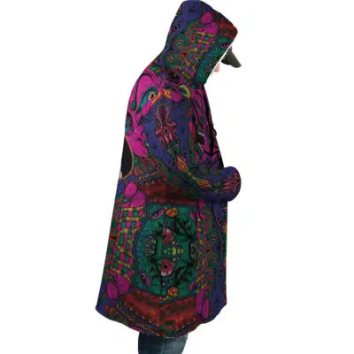 A person wearing the Trippy Mystic Faces Hisoka Hunter X Hunter Dream Cloak Coat, featuring bold abstract patterns in green, purple, pink, and orange, stands in profile with hands in pockets against a white background.