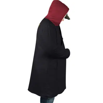 A person wearing the Yuji Itadori Jujutsu Kaisen Dream Cloak Coat, featuring a black body and maroon hood, stands in profile against a white background, looking down with one hand in their pocket and wearing blue jeans.