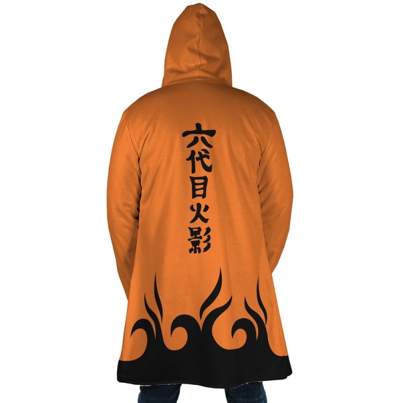 A person stands with their back to the camera, wearing the Hokage Orange Shippuden Dream Cloak Coat featuring black flame patterns at the bottom and vertical Japanese kanji on the back.