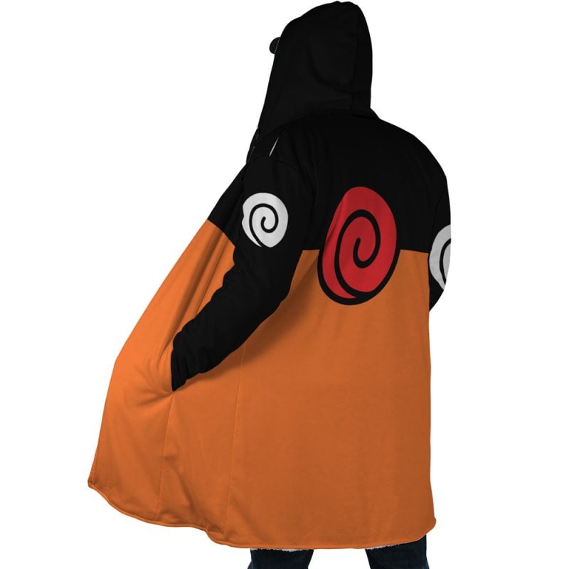 A person wearing the Uzumaki Shippuden Dream Cloak Coat—an orange and black anime-inspired hooded coat with red and white spiral symbols on the back and sleeves—stands with one hand in their pocket.