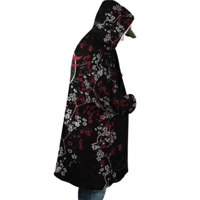 Person wearing the Inarizaki Foxes Haikyuu Dream Cloak Coat, a black hooded coat with striking red and white floral patterns featuring branches and blossoms, standing sideways with hands in pockets and hood up.