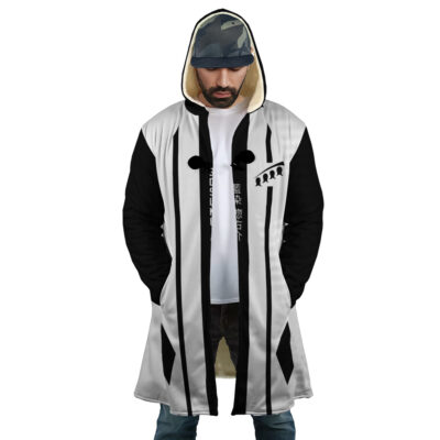 A man wearing the Gotei 13 5th Division Captain Sosuke Aizen Bleach Dream Cloak Coat with a black and white design, his hands in pockets. He sports a short beard, moustache, patterned cap, white T-shirt, and jeans.