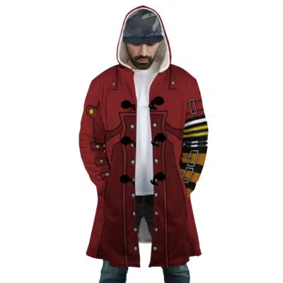 A man stands with hands in pockets, looking down, wearing the Vash the Stampede Trigun Dream Cloak Coat featuring red fabric and black and yellow geometric sleeve designs. He pairs it with a white shirt, blue jeans, and a cap.