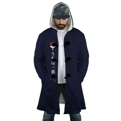 A man stands with hands in pockets, looking down, wearing the Uchiha Clan Sharingan Shippuden Dream Cloak Coat—a dark blue hooded coat with Japanese characters and red-and-white fan symbols—over a white shirt and printed cap.