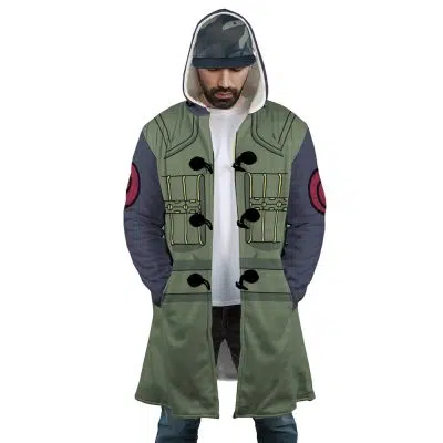 A man wears the Kakashi Hatake Shippuden Dream Cloak Coat, a green and gray anime-style hooded coat with black toggles, pocket details, and red sleeve patches. He pairs it with jeans and a cap.