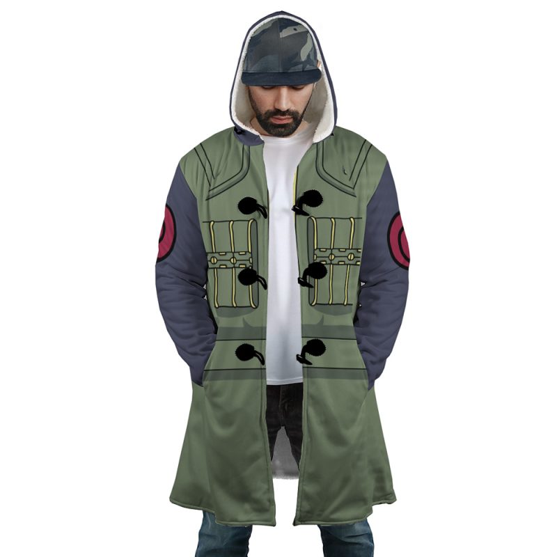 A man wears the Kakashi Hatake Shippuden Dream Cloak Coat, a green and gray anime-style hooded coat with black toggles, pocket details, and red sleeve patches. He pairs it with jeans and a cap.