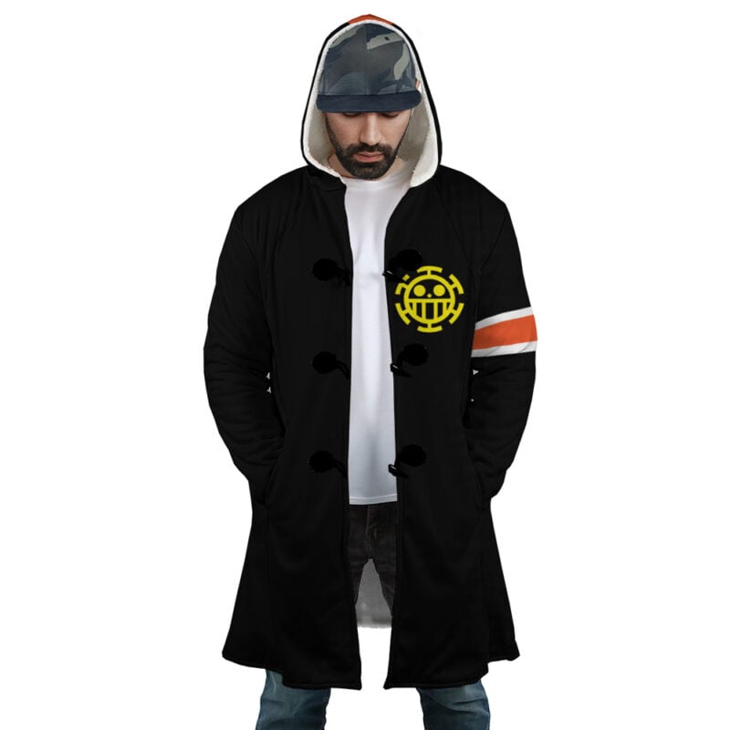 A man wears the Law Timeskip Dressrosa One Piece Corazon Dream Cloak Coat—a black hooded coat with a yellow anchor emblem on the chest, orange-and-white armband, hands in pockets, head bowed, and a cap under the hood.
