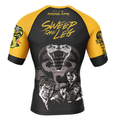 Back view of the Sweep the Leg Cobra Kai Short Sleeve Rash Guard Compression Shirt in black and yellow, with a large cobra, four illustrated men, Japanese text, "SWEEP THE LEG", and sleeve designs including the Cobra logo.
