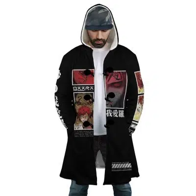 A man wears the Gaara Shippuden Dream Cloak Coat, a long black hooded coat with anime-style graphics and Japanese text in red, white, and black. The design features illustrated faces and dramatic scenes as he looks down with hands in his pockets.
