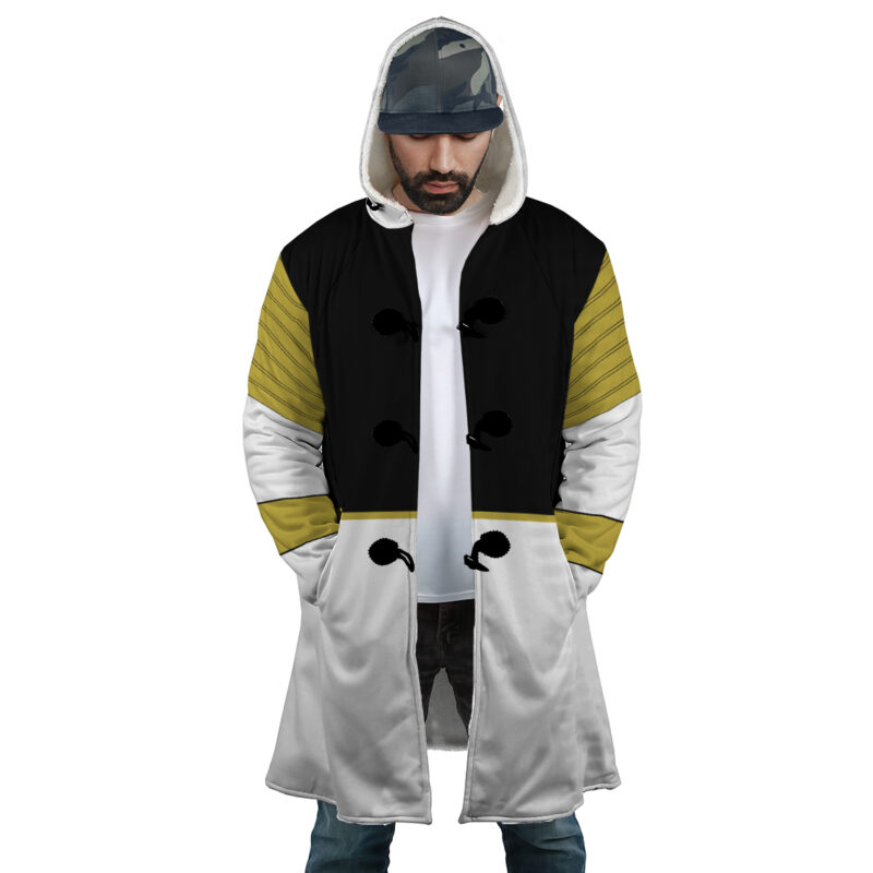 A man wearing the White Ranger Mighty Morphin Power Rangers Dream Cloak Coat, featuring black, white, and olive green sections with decorative black buttons, stands with hands in pockets and head slightly bowed.