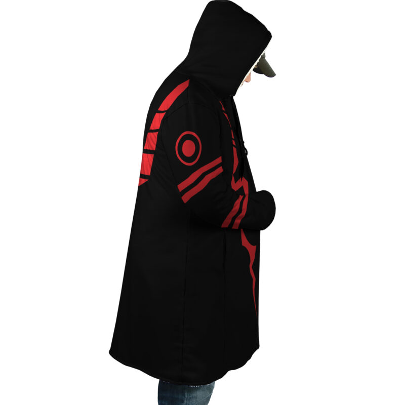 A person stands in profile against a white background wearing the Sukuna Jujutsu Kaisen Dream Cloak Coat, a black hooded coat featuring red designs on the sleeve and side.