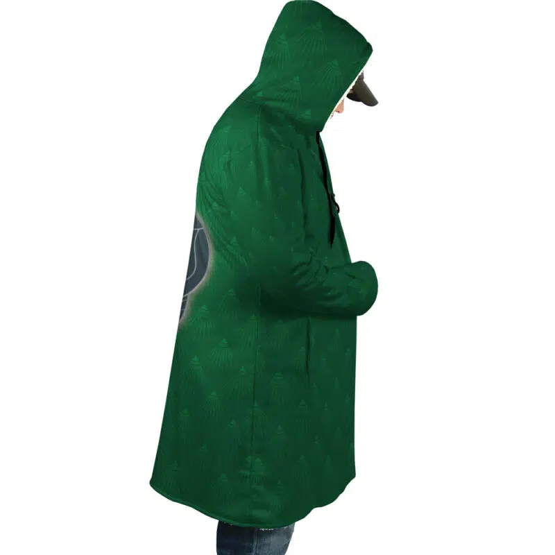 A person in profile wears the Hogwarts Legacy Slytherin Harry Potter Dream Cloak Coat—a long green hooded coat with subtle patterns—plus a cap, hands in the coat pockets, set against a plain white background.