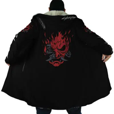 Someone wearing the Johnny Silverhand Cyberpunk 2077 Dream Cloak Coat, featuring a black design with a red and gray flaming demon face and mechanical details on the back, opens the coat to reveal its art. Cyberpunk is written on the collar.