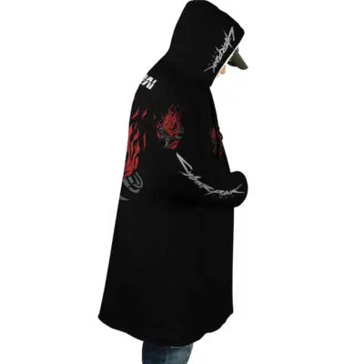 A person stands in profile, hands in pockets, wearing the Johnny Silverhand Cyberpunk 2077 Dream Cloak Coat—a black hooded coat with red dragon designs, white stylized text, and bold graphics on the sleeves and back.
