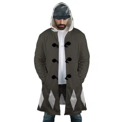 A man wears the Kisuke Urahara Bleach Dream Cloak Coat featuring black fabric, white diamond patterns near the hem, and black toggle buttons, along with a white T-shirt, blue jeans, and a camo baseball cap as he stands with hands in pockets.