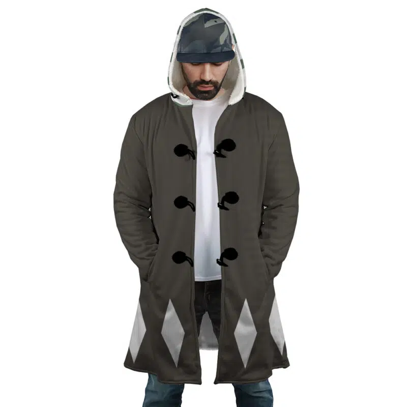 A man wears the Kisuke Urahara Bleach Dream Cloak Coat featuring black fabric, white diamond patterns near the hem, and black toggle buttons, along with a white T-shirt, blue jeans, and a camo baseball cap as he stands with hands in pockets.