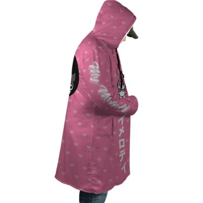 A person is wearing the My Melody and Kuromi Sanrio Dream Cloak Coat, featuring pink fabric with small white hearts, My Melody graphics, and white Japanese text on the sleeve and front, facing sideways with hands in pockets.