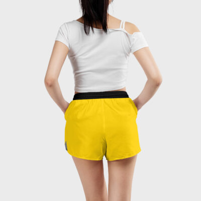 A woman stands facing away, wearing a white off-shoulder crop top and Trafalgar Law One Piece Women's Board Shorts with a black waistband, hands in her pockets, against a plain light gray background.