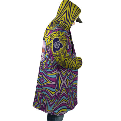 A person in profile wears the Trippy The Cream of the Crop Randy Savage Dream Cloak Coat, a hooded jacket with bold psychedelic yellow, purple, and blue geometric patterns and a skull patch on the sleeve, set against a white background.