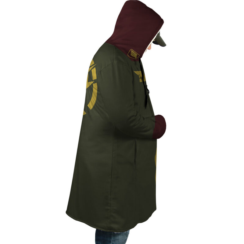 A person models the Zeon Uniform Gundam Dream Cloak Coat—a long, dark green and maroon hooded coat with gold designs on the sleeves and back—standing in profile with hands in pockets, looking down.