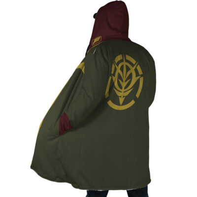 A person wearing the Zeon Uniform Gundam Dream Cloak Coat, featuring a green and maroon hood with a yellow stylized wheat emblem and circular designs on the back, stands with one hand in the pocket, facing away from the camera.