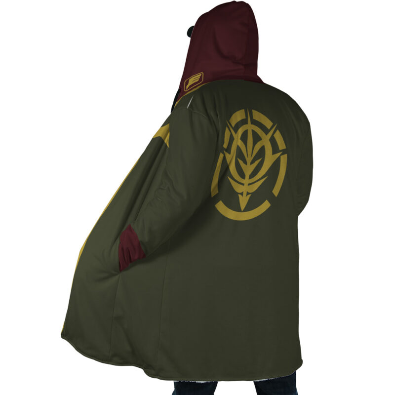A person wearing the Zeon Uniform Gundam Dream Cloak Coat, featuring a green and maroon hood with a yellow stylized wheat emblem and circular designs on the back, stands with one hand in the pocket, facing away from the camera.