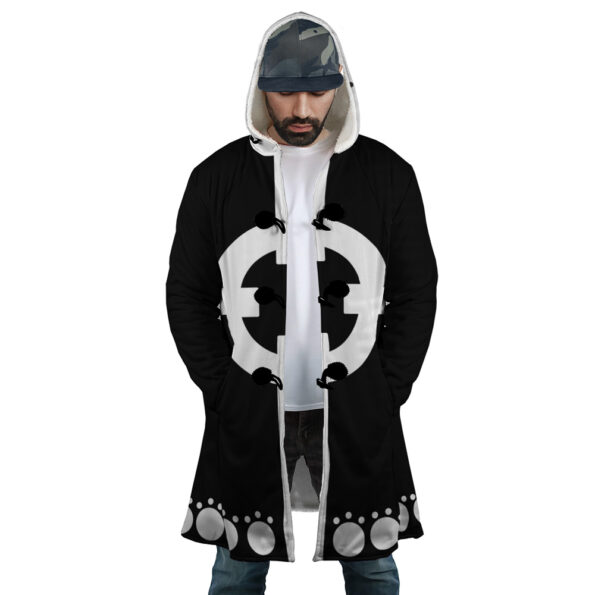 A man wearing a black and white hooded coat with a bold circular symbol on the front and a pattern of gray circles along the bottom, standing with his hands in his pockets and looking down.