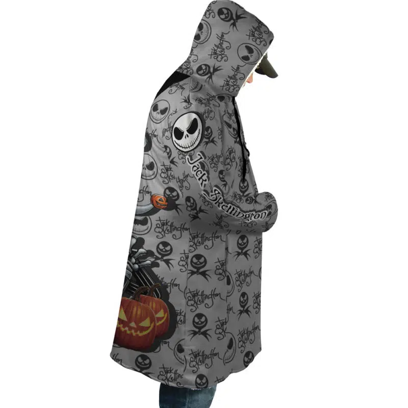 A person wearing the Jack Skellington The Nightmare Before Christmas Dream Cloak Coat, featuring a gray design with Jack Skellington, black bats, and orange pumpkins, faces sideways with their head slightly bowed.