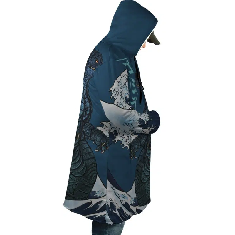 Wearing the Godzilla Dream Cloak Coat, featuring a blue hood, wave patterns, and a Godzilla-like sea monster design, a person stands in profile with hands in their pockets, gazing downward.