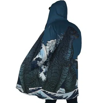 A person wears the Godzilla Dream Cloak Coat, which features a large, detailed illustration of Godzilla emerging from ocean waves against a stormy blue and white background.