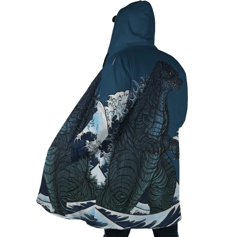 A person wears the Godzilla Dream Cloak Coat, which features a large, detailed illustration of Godzilla emerging from ocean waves against a stormy blue and white background.
