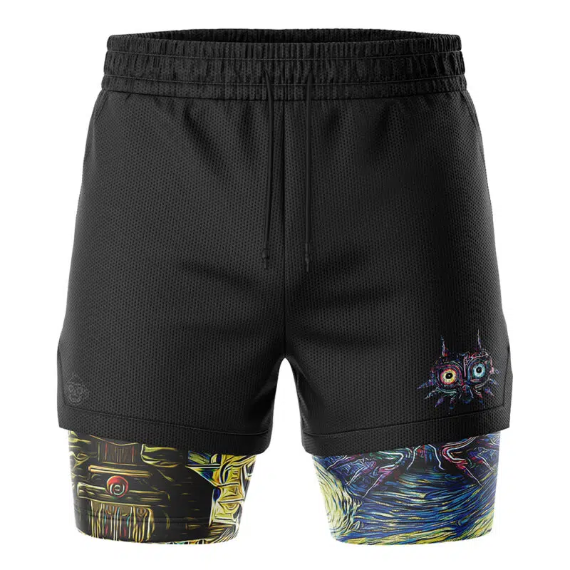 The Zelda Majora's Mask Starry Night 2-in-1 Performance Shorts feature black outer shorts with a drawstring waistband and a colorful abstract cat face on the left leg, revealing multicolored geometric patterned compression shorts underneath.