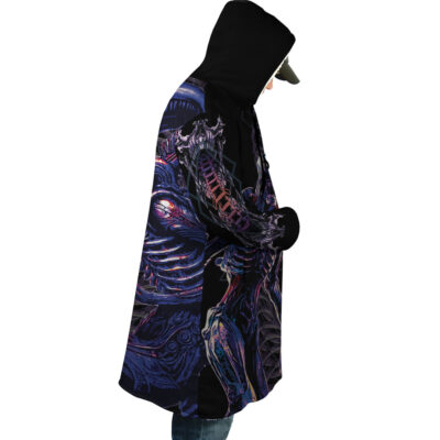 A person in a Yautja Predator Dream Cloak Coat stands in profile against a white background, wearing blue jeans and a cap under the hood. The coat features a large, colorful, sci-fi creature design.