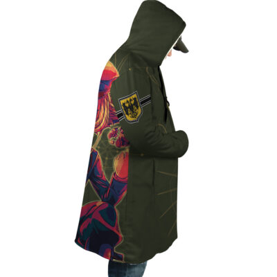 A person wears the Nero Devil May Cry 4 Dream Cloak Coat, an olive-green hooded coat featuring a vibrant anime character on the side and a yellow patch with black symbols on the upper arm, standing in profile with hands in pockets.