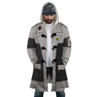 A man wears the Sidon The Legend of Zelda Dream Cloak Coat—a long, gray hooded coat with black accents and decorative patches—over a white t-shirt and camouflage cap, standing with his hands in his coat pockets.