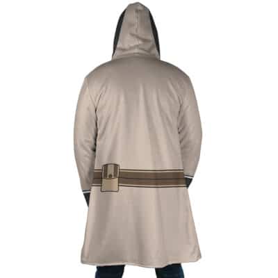 A person wearing the Cid Kageno Shadow Cosplay The Eminence in Shadow Dream Cloak Coat, which is long, beige, hooded, and features a brown belt graphic on the back, stands with their back to the camera.