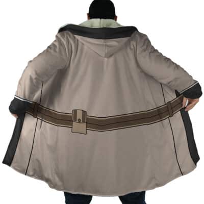 A person models the Cid Kageno Shadow Cosplay Dream Cloak Coat, featuring a tan hood, brown cartoon-style belt print on the back, and dark inner lining. The coat is held open to show its design; the wearer’s face is hidden.