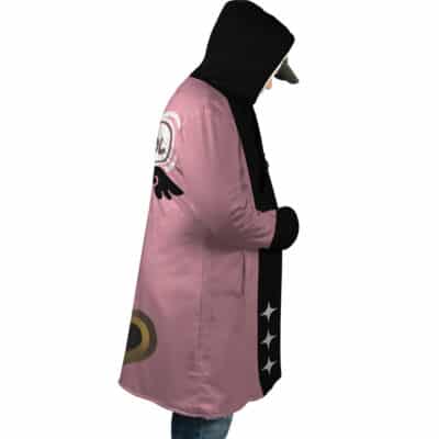 A person wears the Belle Vibrant Store Manager Zenless Zone Zero Dream Cloak Coat, featuring pink and black colors with graphic designs like black wings, a target symbol, and white stars, styled with a cap and jeans, standing in profile hands in pockets.