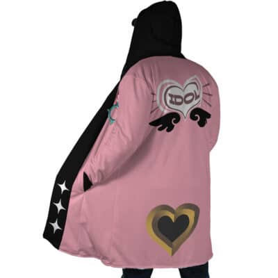 A person wears the Belle Vibrant Store Manager Zenless Zone Zero Dream Cloak Coat, a long pink and black hooded coat decorated with hearts, wings, stars, and a large winged heart with "IDOL" on the back plus a gold heart near the hem.