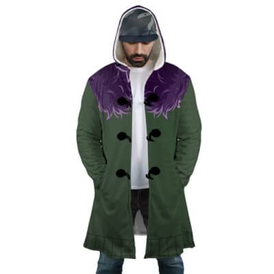 A man wearing the Shinigami Death Seal Shippuden Dream Cloak Coat with a purple, fur-like collar, black buttons, white shirt, black pants, and a cap stands looking down with his hands in his coat pockets.